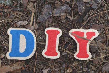 Three colorful wooden letters spelling "DIY" are placed on a rustic forest floor covered with pine needles and dry leaves. This image is ideal for illustrating concepts of hobbies, craftsmanship, home improvement, or self-sufficiency.の写真素材