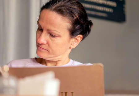 A middle-aged caucasian woman in a restaurant reads the menu and chooses dishes.の写真素材