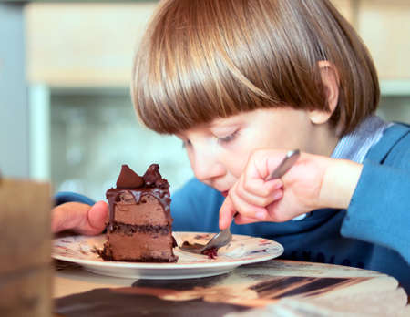 A caucasian boy in a restaurant eats piece of chocolate cake by fork.の写真素材
