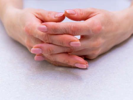 The girl's hands with extended manicure on a bright table with intertwined fingers.の写真素材