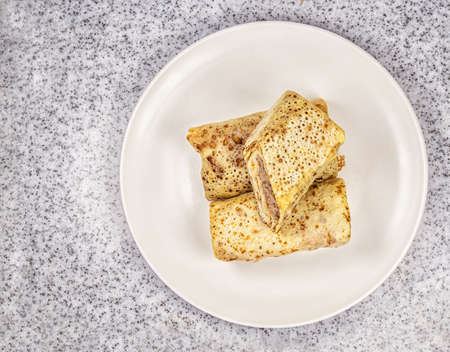 The homemdade pancakes filled by meat on the white plate on the marble countertop table.