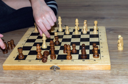 The hands of unknown a caucasian boy who is playing chess on a wooden floor. Close up.