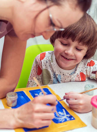 Caucasian boy with his mom are drawing with gouache a drawing. Homeschooling. Selective focus. Close-up.の写真素材