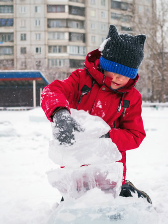 Caucasian boy in a red jacket in winter plays with ice floes in the city.の写真素材