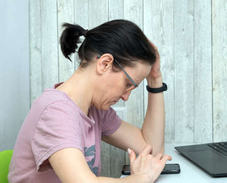 A middle aged woman in casual clothes is working remotely in her home office. Using laptop and...