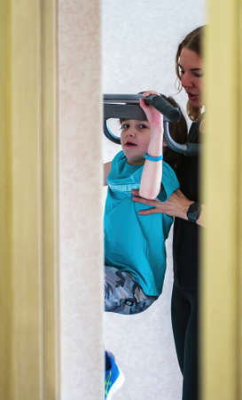 An eight-year-old boy goes in for sports with an instructor on strength simulators. Double portrait....