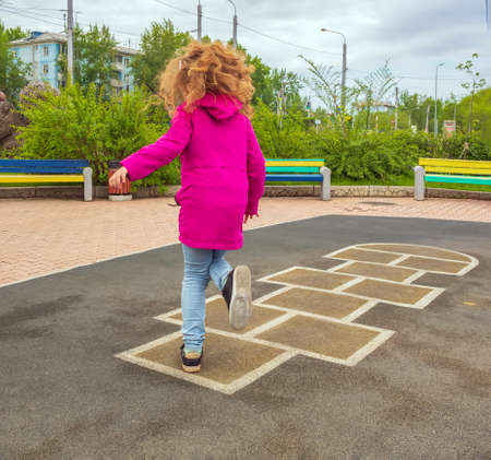 Redhead girl playing hopscotch on school playground. Back view. No faces.の写真素材
