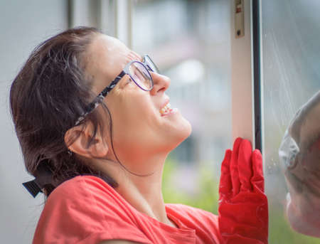 Caucasian woman middle-age casual wear is washing windows in apartment. Close-up. Cleaning house,...