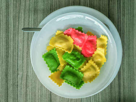 White plate of multi-colored ravioli is standing on a wooden table. Close-up.の写真素材
