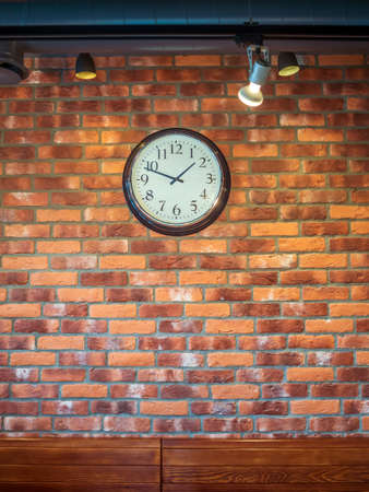 The wall clock hangs on a red-brick wall.の写真素材