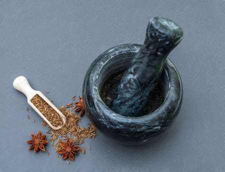 Malachite mortar with caraway seeds and anise stars on a gray background.