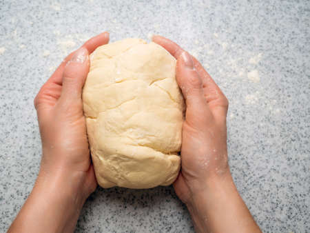 Hands of a young girl is holding a lump of dough in the palms. Top view, close-up.の写真素材
