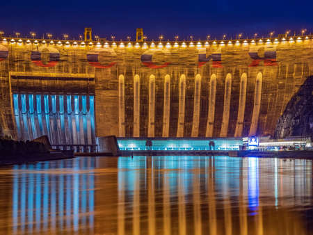 Night picture of 800 fts arched concrete dam of hydroelectric power station. Reflecting lights in the river.の写真素材