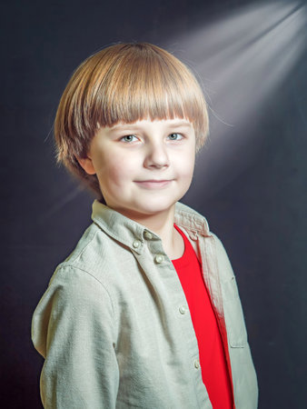 Portrait of caucasian ten-years-boy wearing gray shirt and red undershirt looking at the camera on the dark background with falling rays of light from the upper right corner.の写真素材