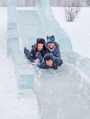 Three boys are rolling down an ice slide outdoors in winter. Childhood, fun and joy.の写真素材