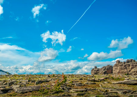 Contrail of an airplane flying in a clear blue sky over the rocky arctic tundra