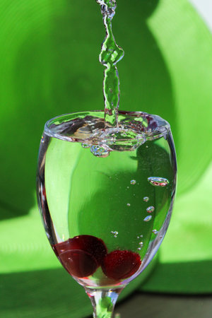 Glittering splashes of water that appeared in a glass of water after frozen berries were thrown into it. The splashes sparkle on in the sunlight.の写真素材