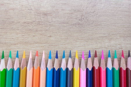 A lot of multi-colored bright pencils in an even row on a wooden backgroundの写真素材