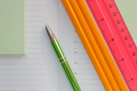 Close-up of an open diary for writing, a green pen, three orange pencils and a pink ruler with a...