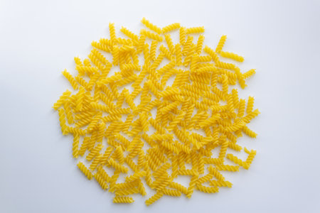 Yellow spiral pasta laid out in circle shape on white backgroundの写真素材