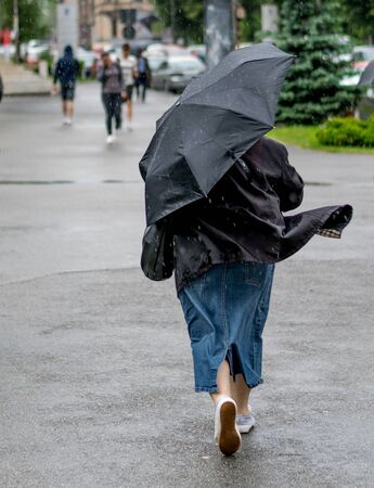 SIBIU, ROMANIA - 24 APRIL 2016: older woman waking with an umbrella in a windy rain in Sibiu, Romaniaのeditorial素材