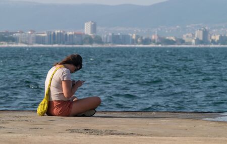 Nessebar, Bulgaria - 2 Sep 2018: Single woman looking at a phone with sea in the background.のeditorial素材