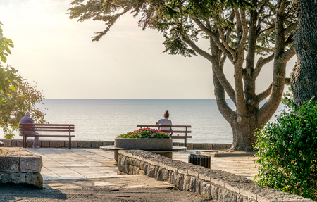 Unidentifiable people on a bench looking peacefully at the see in Nessebar ancient city on the Bulgarian Black Sea Coast.の写真素材