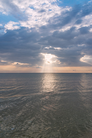 Sunbeams or sun rays peeking through the clouds at a sunrise at sea.の写真素材