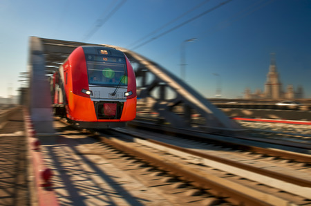bright red high-speed passenger train leaves the tunnel bridge. In the background high-rise building. High speed blurs of silhouettesの写真素材