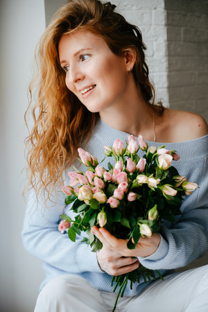 Portrait of a young beautiful girl with a bouquet of roses near window.の写真素材