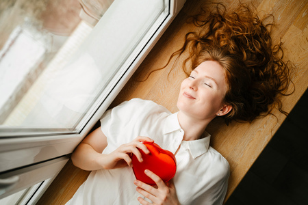 Beautiful young girl lying by the window with a gift for Valentines day.の写真素材
