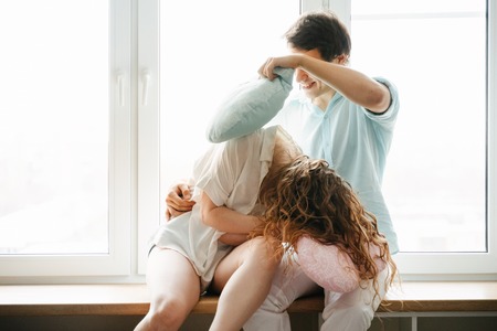 Couple girl and guy play with pillows near window.の写真素材
