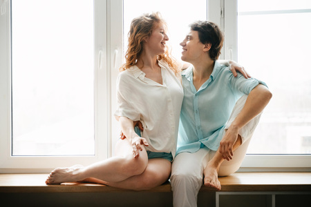 Happy girl and man hugging near window in home.の写真素材