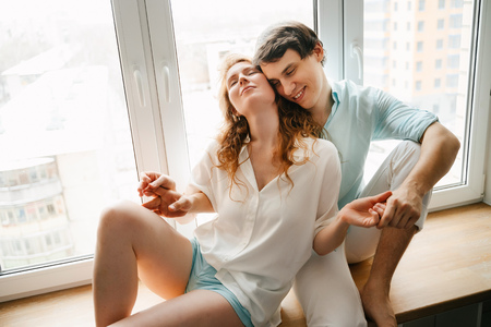Happy girl and man hugging near window in home.の写真素材
