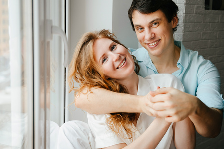 Happy girl and man hugging near window in home.の写真素材