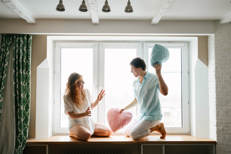 Couple girl and guy play with pillows near window.の写真素材