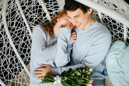 Couple girl and guy hugging on a big chair with a bouquet of roses.の写真素材