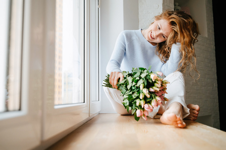 Portrait of a young beautiful girl with a bouquet of roses near window.の写真素材