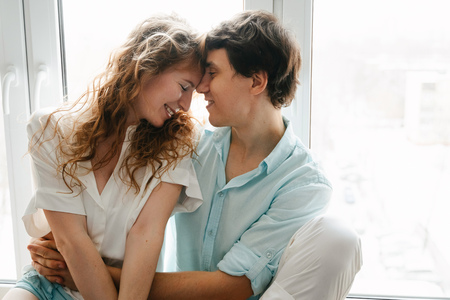 Happy girl and man kissing near window in home.の写真素材