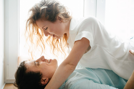 Happy girl and man hugging near window in home.の写真素材