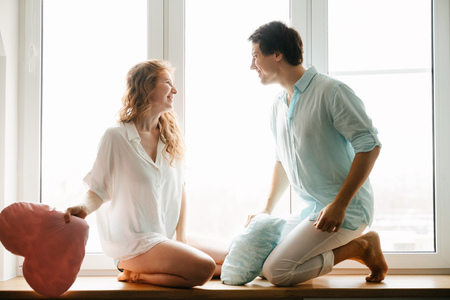 Couple girl and guy play with pillows near window.の写真素材