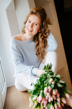Portrait of a young beautiful girl with a bouquet of roses near window.の写真素材