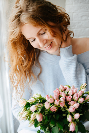 Portrait of a young beautiful girl with a bouquet of roses near window.の写真素材