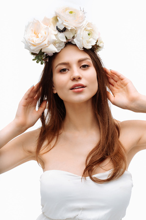 Beautiful young girl smiling and posing with flowers on white background in white dress. Studio portrait.の写真素材