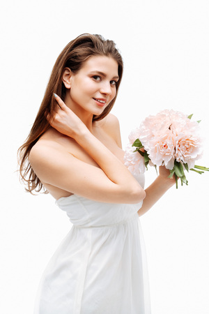 Portrait beautiful young girl smiling and posing with artificial flowers on white background in white dress.の写真素材