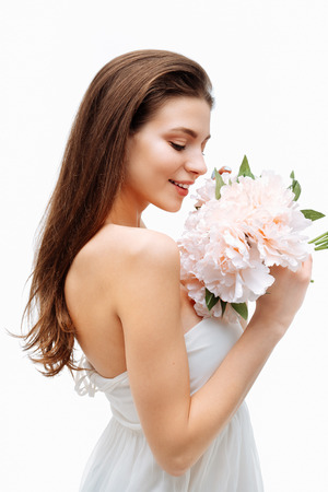 Portrait beautiful young girl smiling and posing with artificial flowers on white background in white dress.の写真素材
