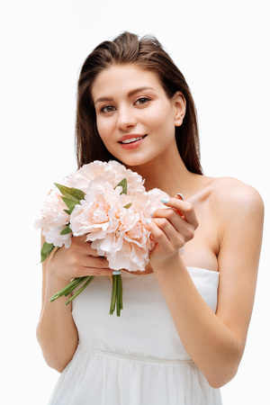 Portrait beautiful young girl smiling and posing with artificial flowers on white background in white dress.の写真素材
