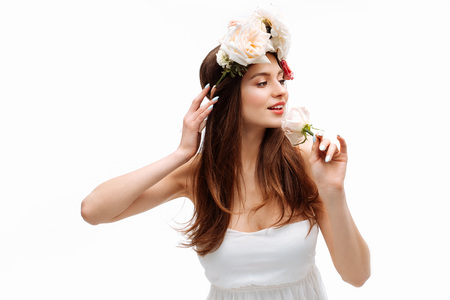 Beautiful young girl smiling and posing with flowers on white background in white dress. Studio portrait.の写真素材