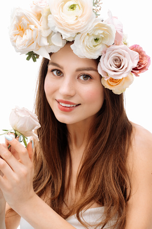 Beautiful young girl smiling and posing with flowers on white background in white dress. Studio portrait.の写真素材