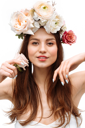 Beautiful young girl smiling and posing with flowers on white background in white dress. Studio portrait.の写真素材
